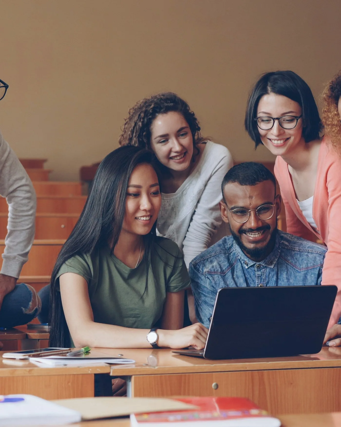 A diverse group of students gathered around a laptop, working together